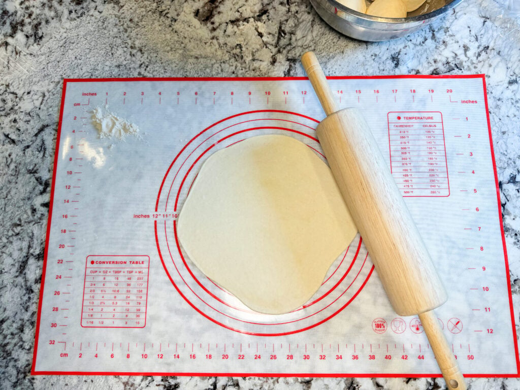 photo of tortilla dough being rolled out by a roller