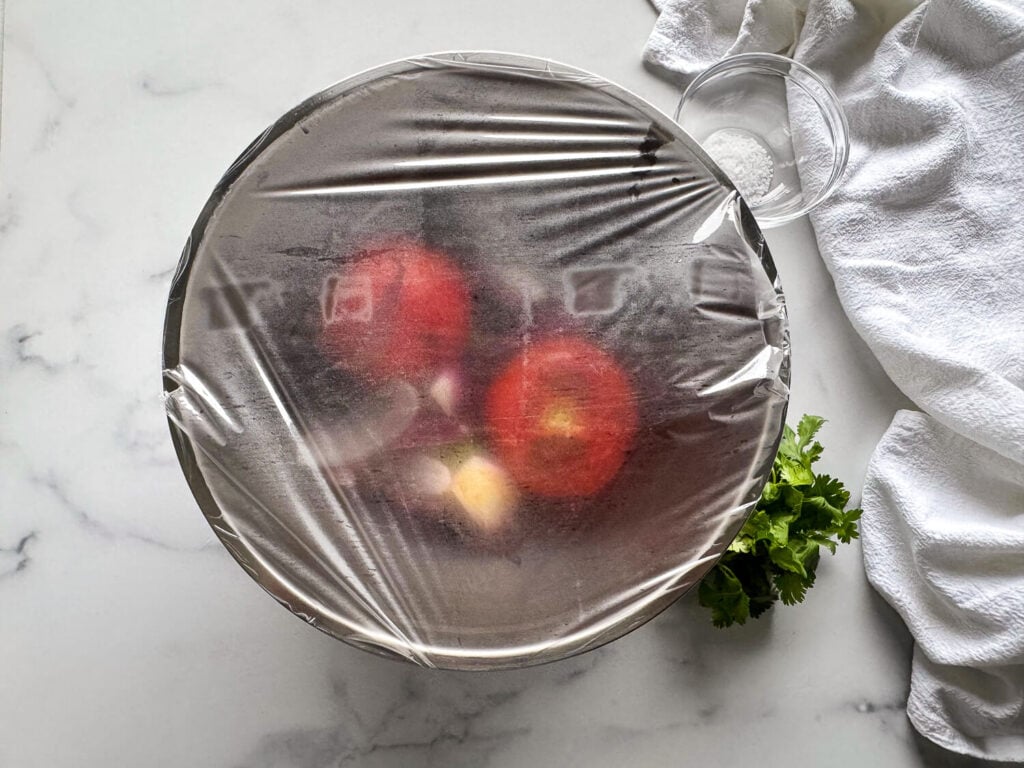 photo of tomatoes-onions and-garlic in a bowl covered in plastic to steam