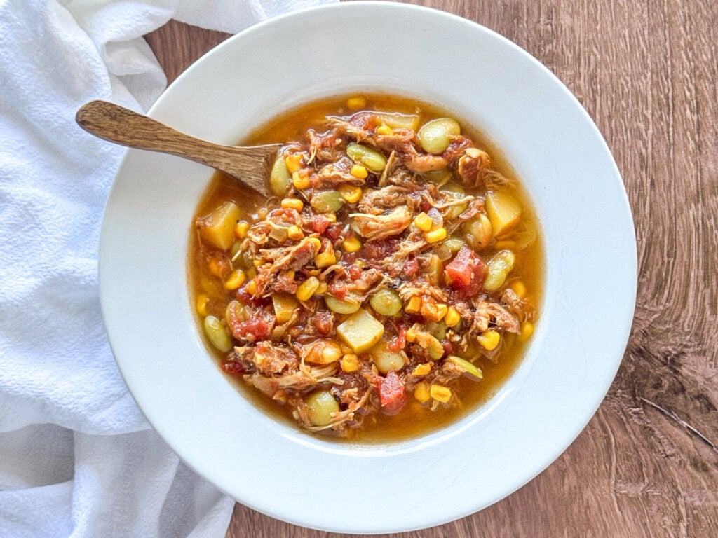 overhead shot of Brunswick Stew in a white bowl with a wooden spoon