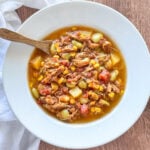 overhead shot of Brunswick Stew in a white bowl with a wooden spoon