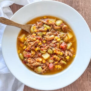 overhead shot of Brunswick Stew in a white bowl with a wooden spoon