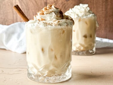 photo of two glasses of dairy-free eggnog topped with dairy-free whipped cream and nutmeg