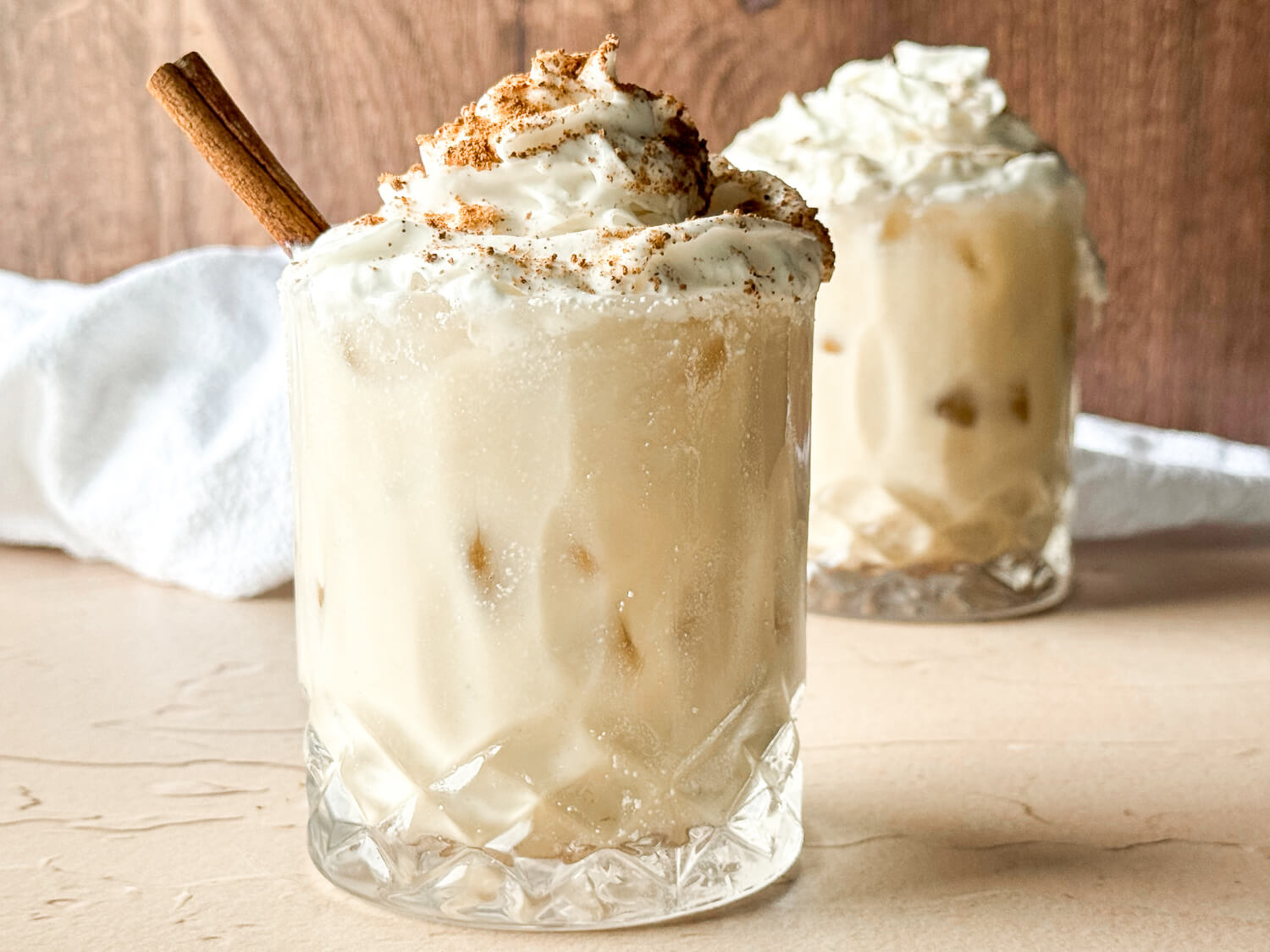 photo of two glasses of dairy-free eggnog topped with dairy-free whipped cream and nutmeg