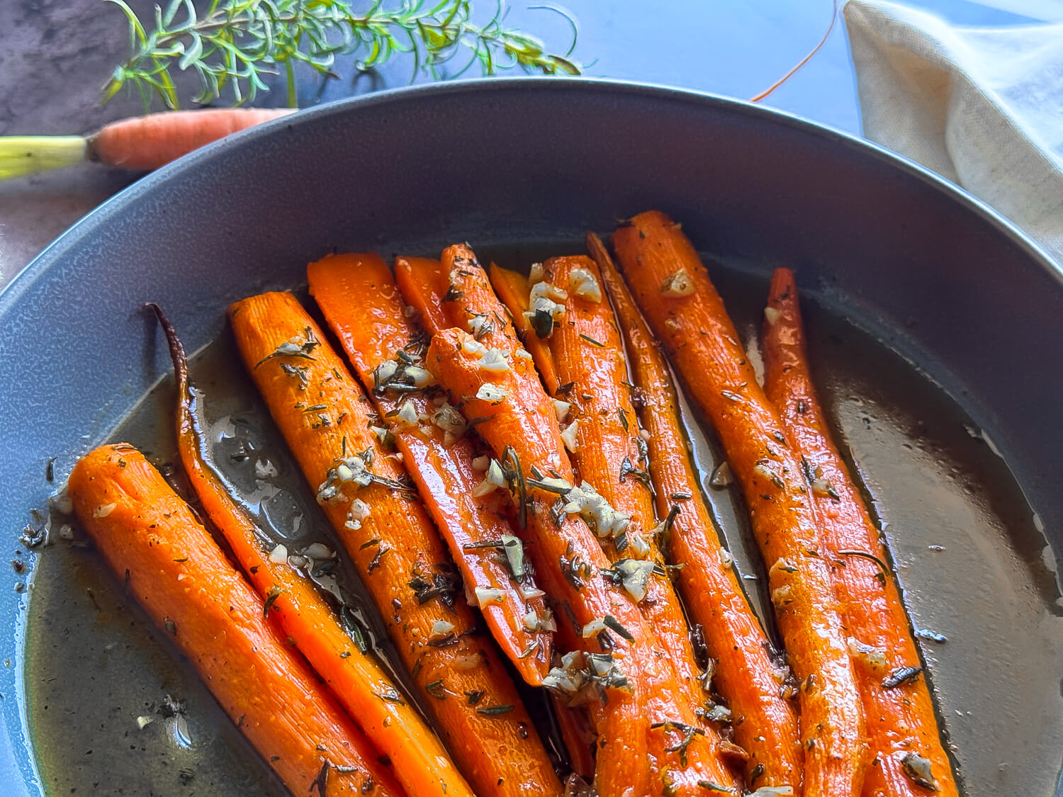 photo of honey roasted carrots in a gray bowl garnished with rosemary