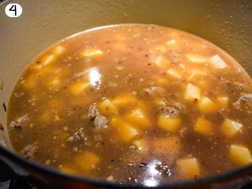 photo of chicken broth and potatoes being added to make Zuppa Toscana soup