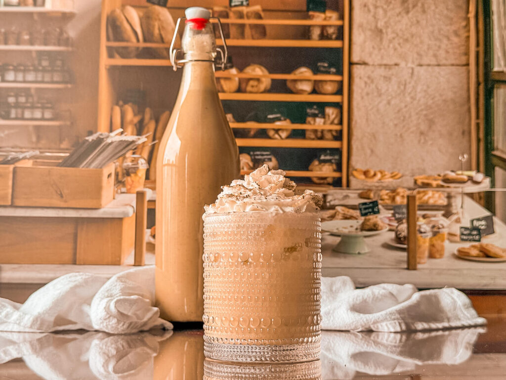 photo of two glasses of dairy-free eggnog topped with dairy-free whipped cream next to an airtight bottle
