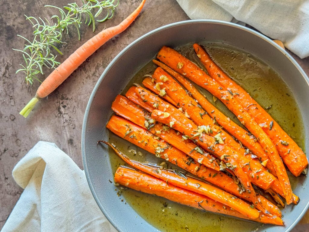 photo of honey roasted carrots in a gray bowl garnished with rosemary