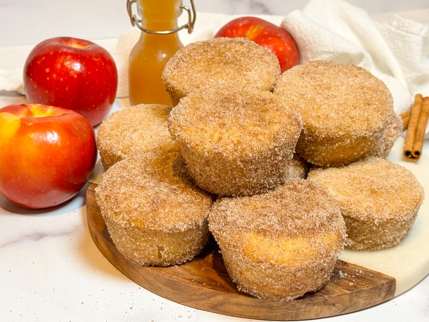 photo of Apple Cider Muffins stacked on top of each other next to apple cider and apples