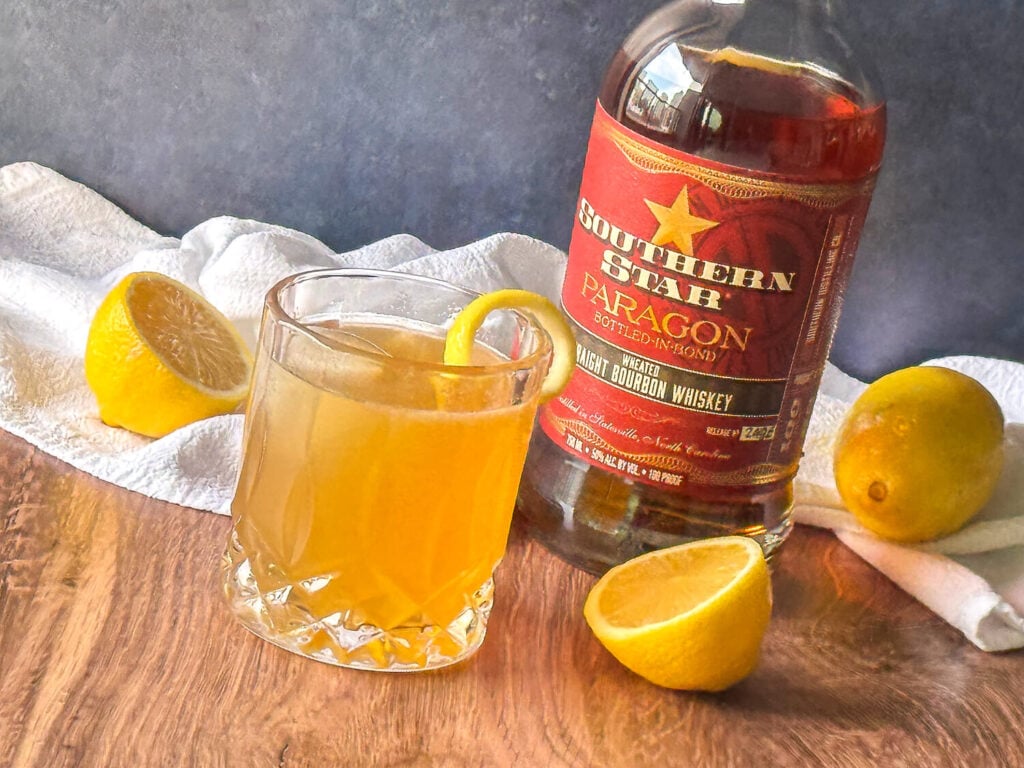 photo of Gold Rush Cocktail next to a bourbon bottle