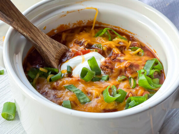 close up photo of chili with cheese sour cream and green onions
