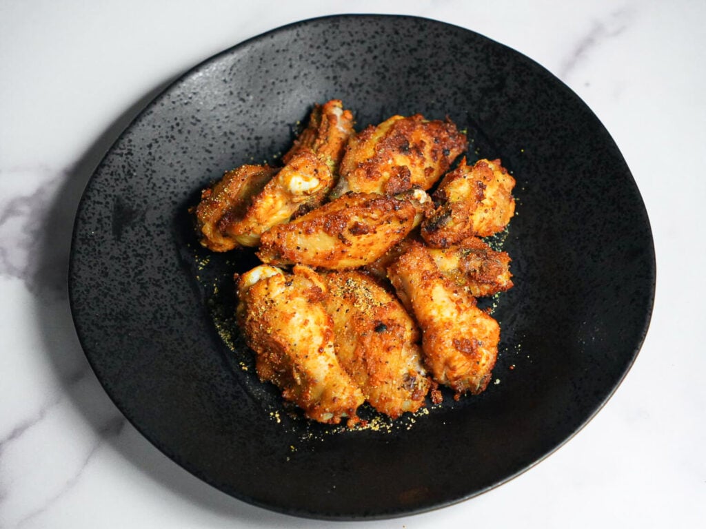Air Fryer Lemon Pepper Wings on a black plate with lemon pepper seasoning on top