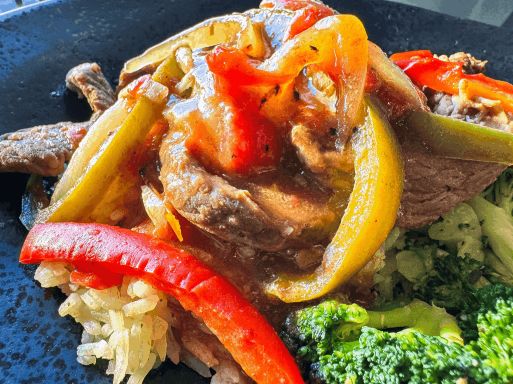 Close up photo of cooked steak and glazed peppers on rice and broccoli