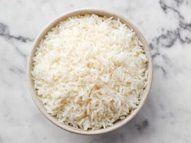 photo of cooked white rice in a tan bowl on a marble surface