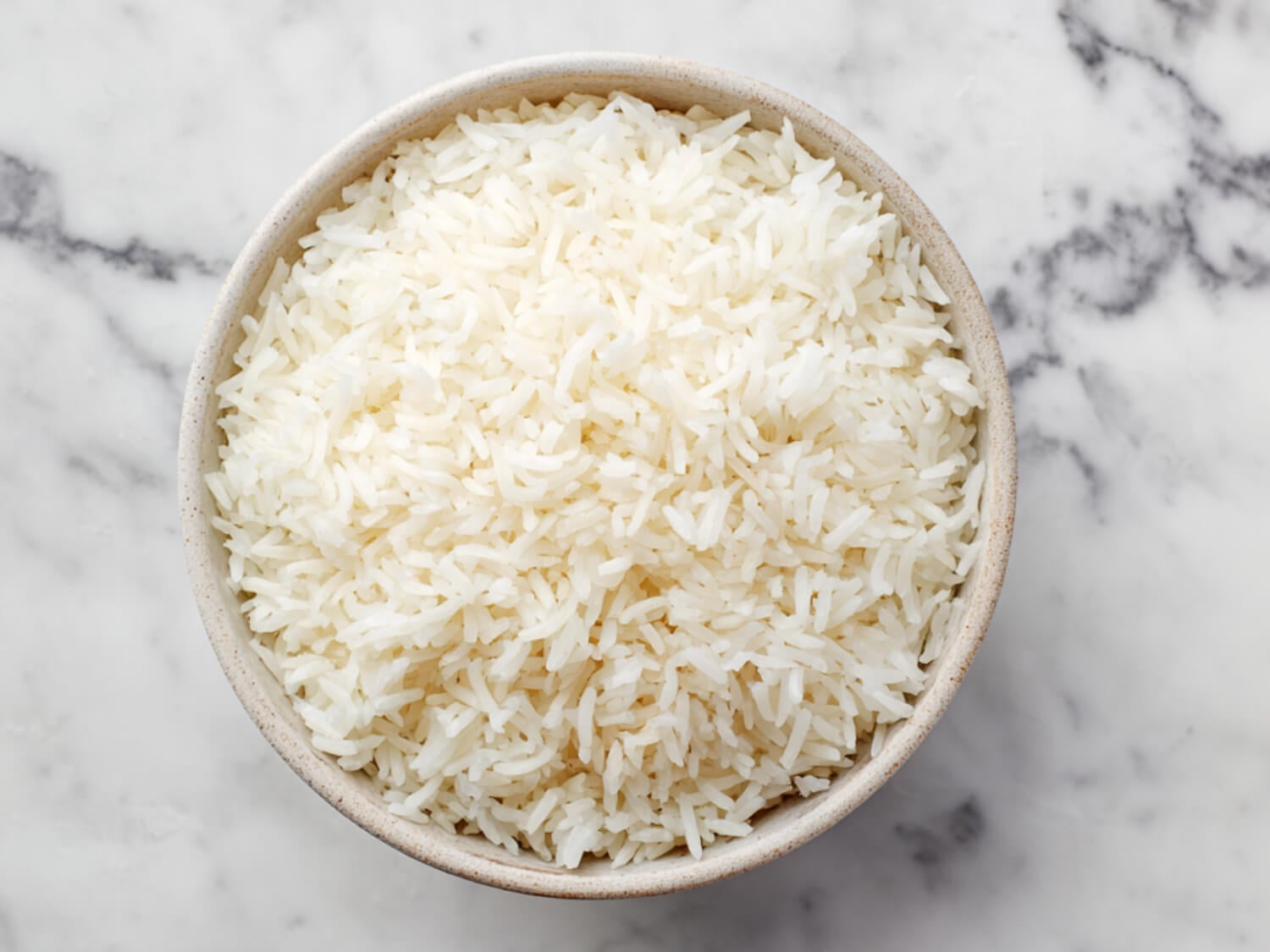 photo of cooked white rice in a tan bowl on a marble surface
