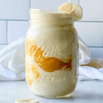 Close up photo of a peanut butter smoothie in a mason jar garnished with a banana slice