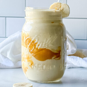 Close up photo of a peanut butter smoothie in a mason jar garnished with a banana slice