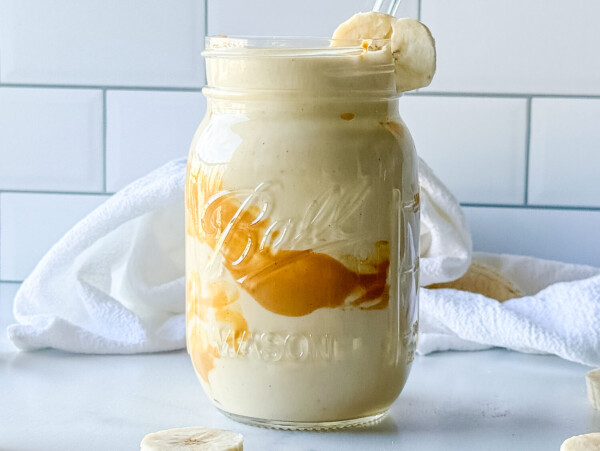 Close up photo of a peanut butter smoothie in a mason jar garnished with a banana slice