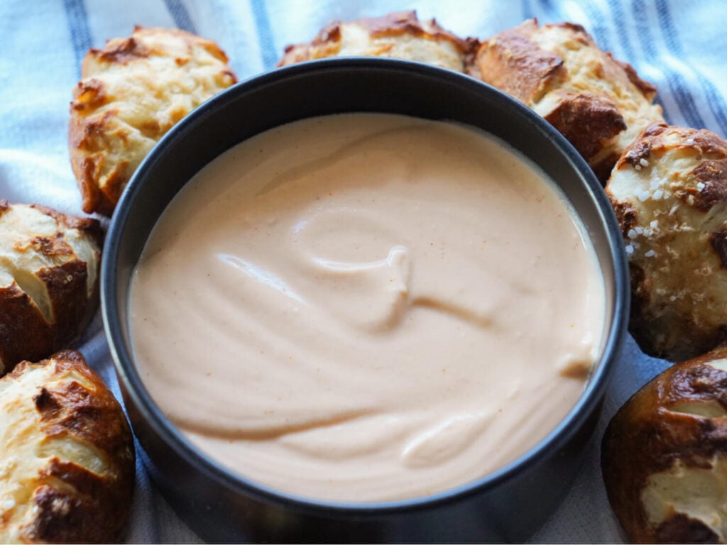 a photo of beer cheese dip in a black bowl surrounded by pretzel buns