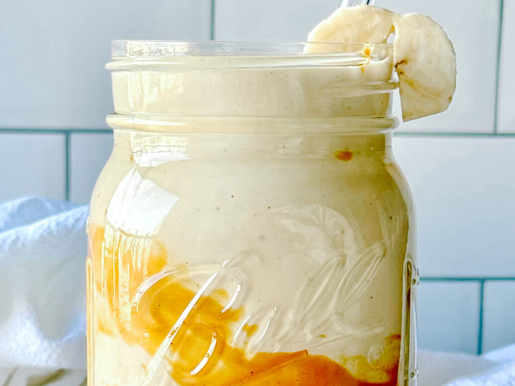 Close up photo of a peanut butter smoothie in a mason jar garnished with a banana slice