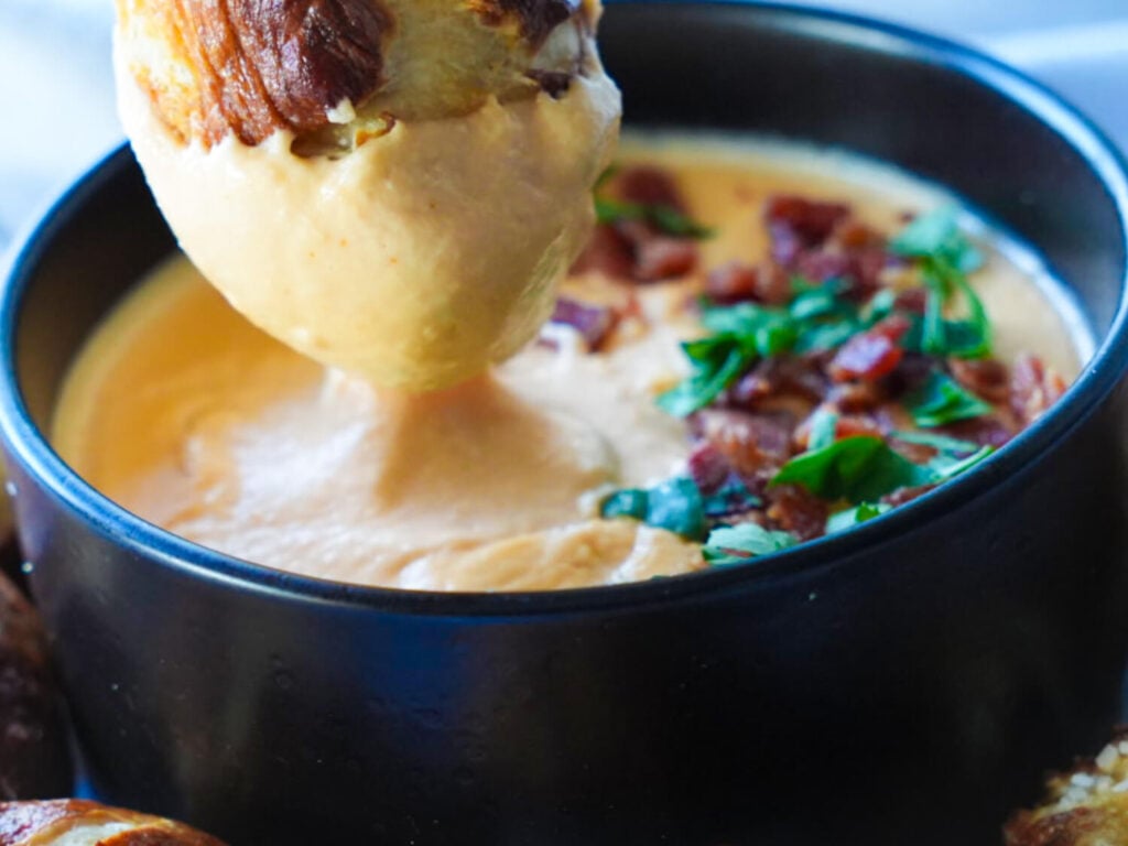 close up photo of pretzel being dipped in beer cheese