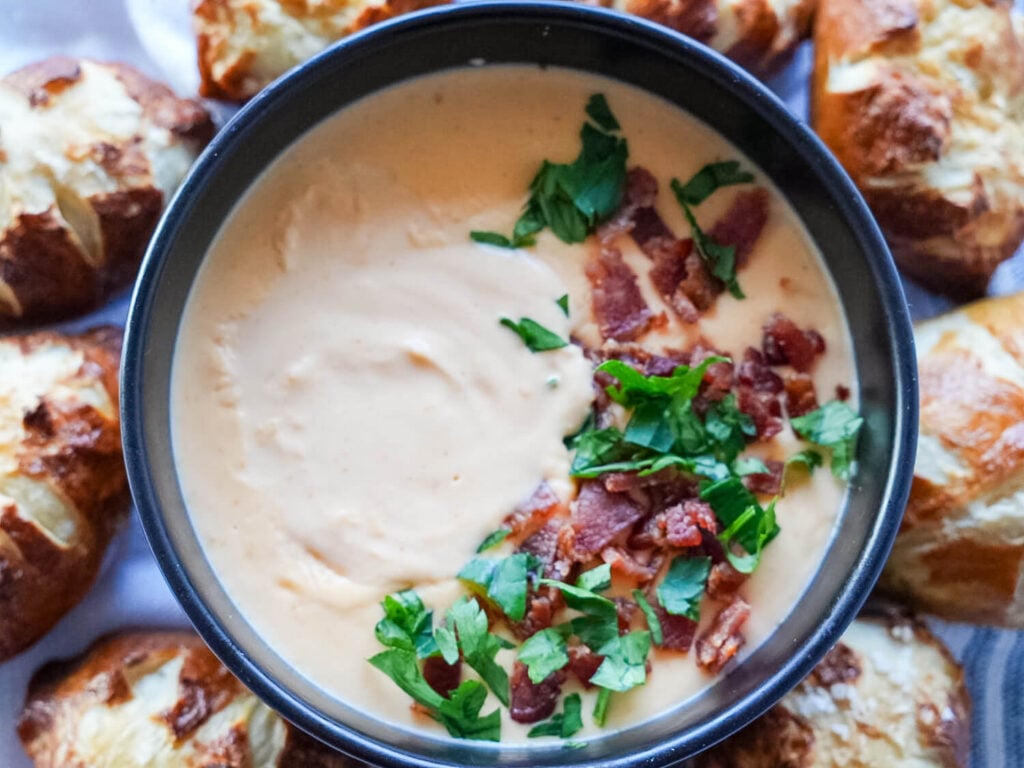 overhead photo of beer cheese dip surrounded by pretzels and garnished with bacon and parsley
