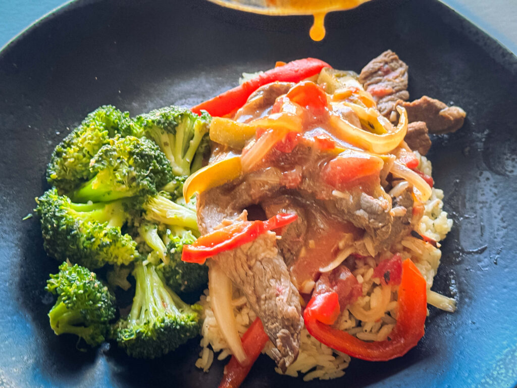 photo of gravy dripping on top of the pepper steak that's resting on rice