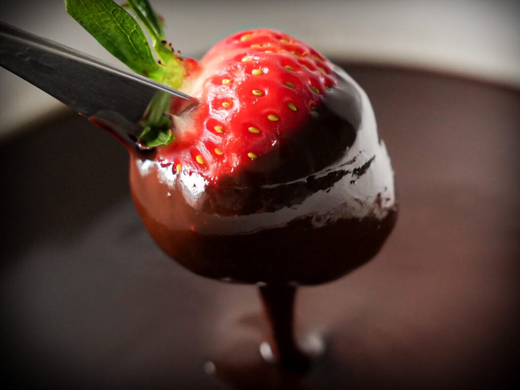Close up photo of a strawberry being dipped in chocolate fondue