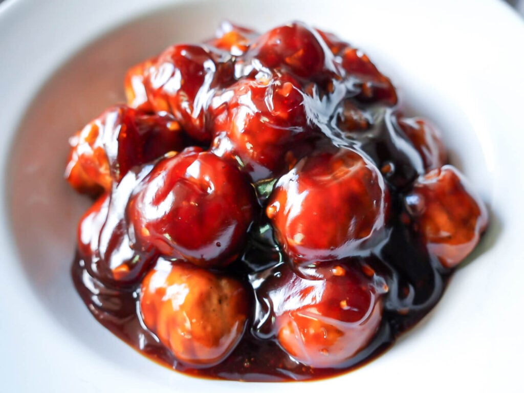 Close up photo of meatballs in a white bowl glazed with honey garlic sauce