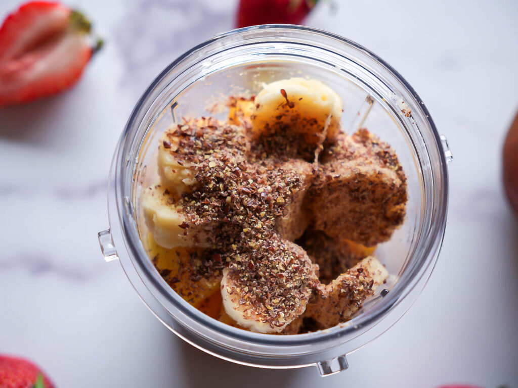 Overhead photo of ingredients in a blender cup with flaxseed on top