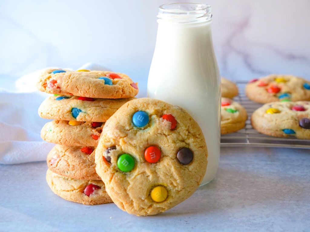 Photo of M&M cookies stacked next to a bottle of milk