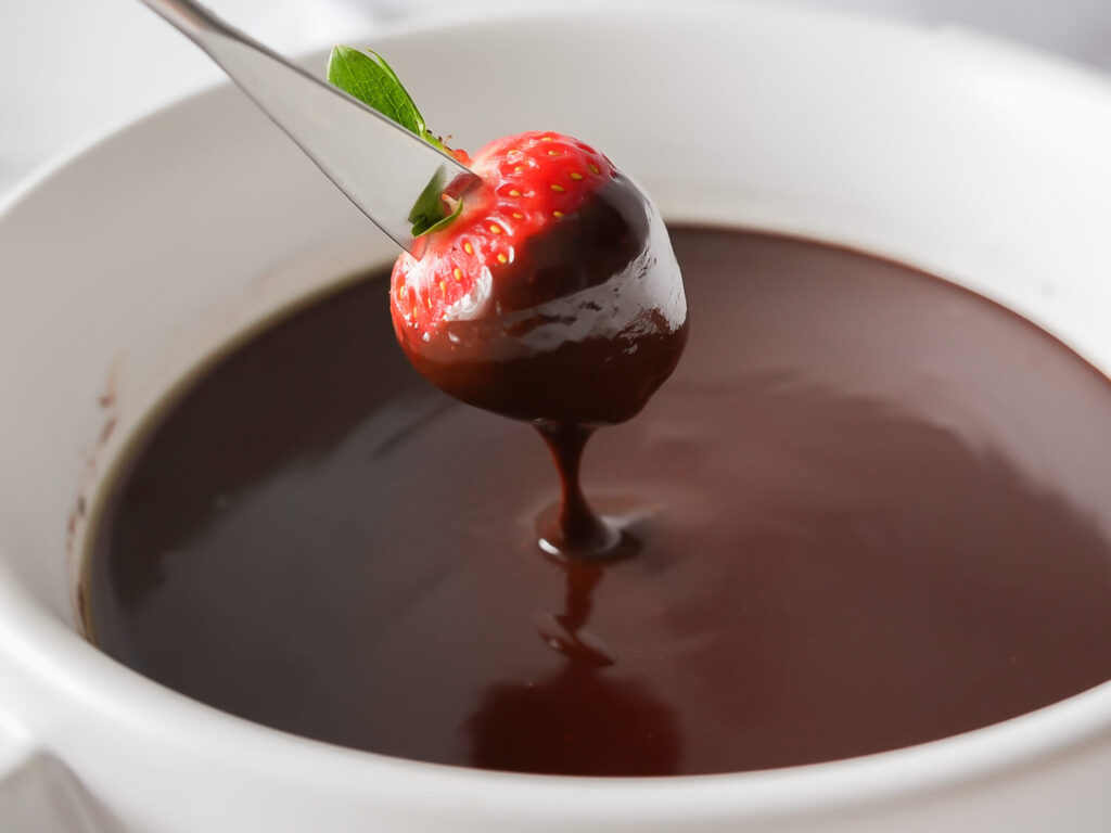 Side view photo of a strawberry being dipped in chocolate fondue