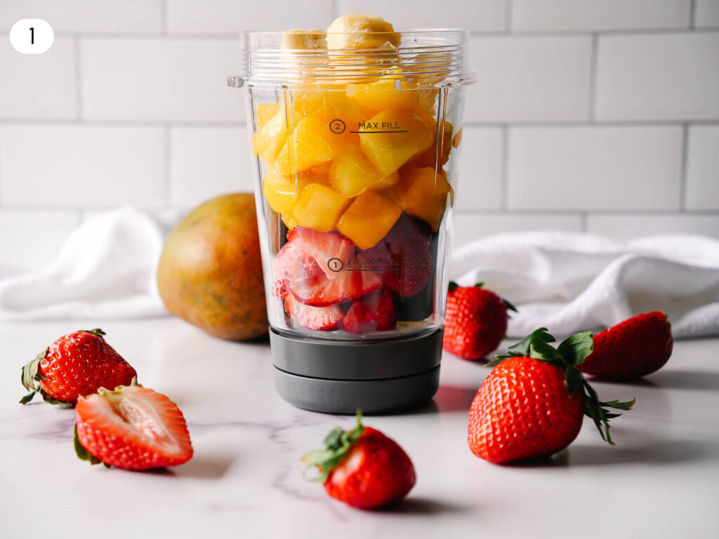 Step 1 photo of strawberry mango smoothie ingredients being added to a blender