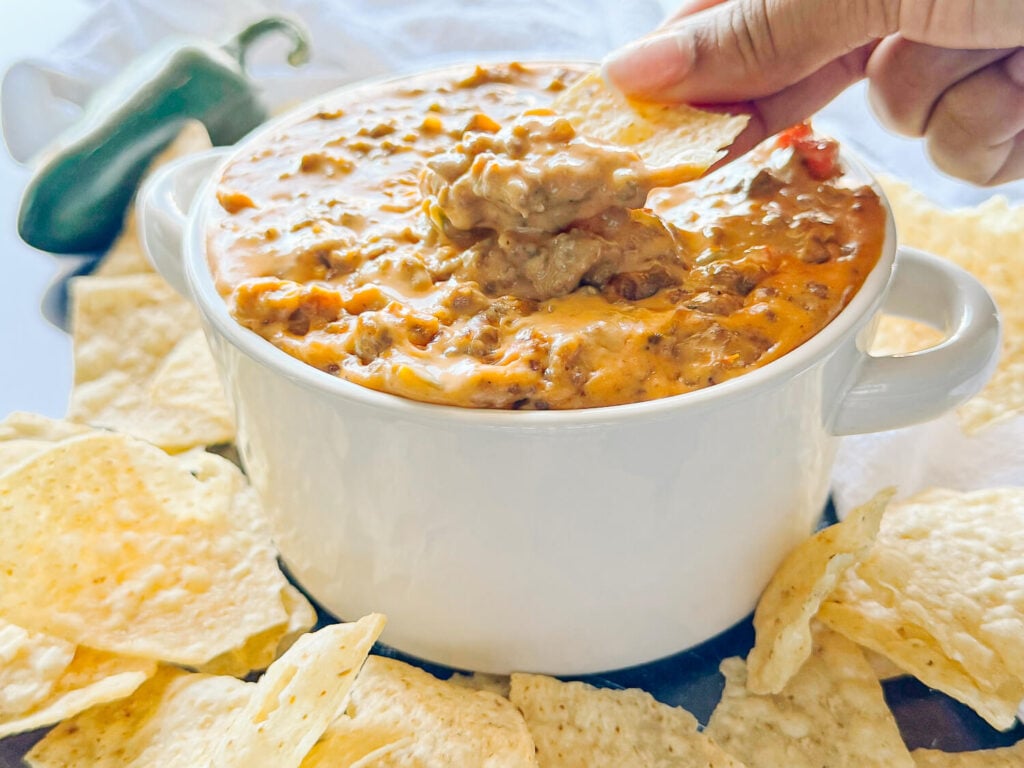 action photo of scooping Sausage Cheese Dip with a tortilla chip in a white bowl