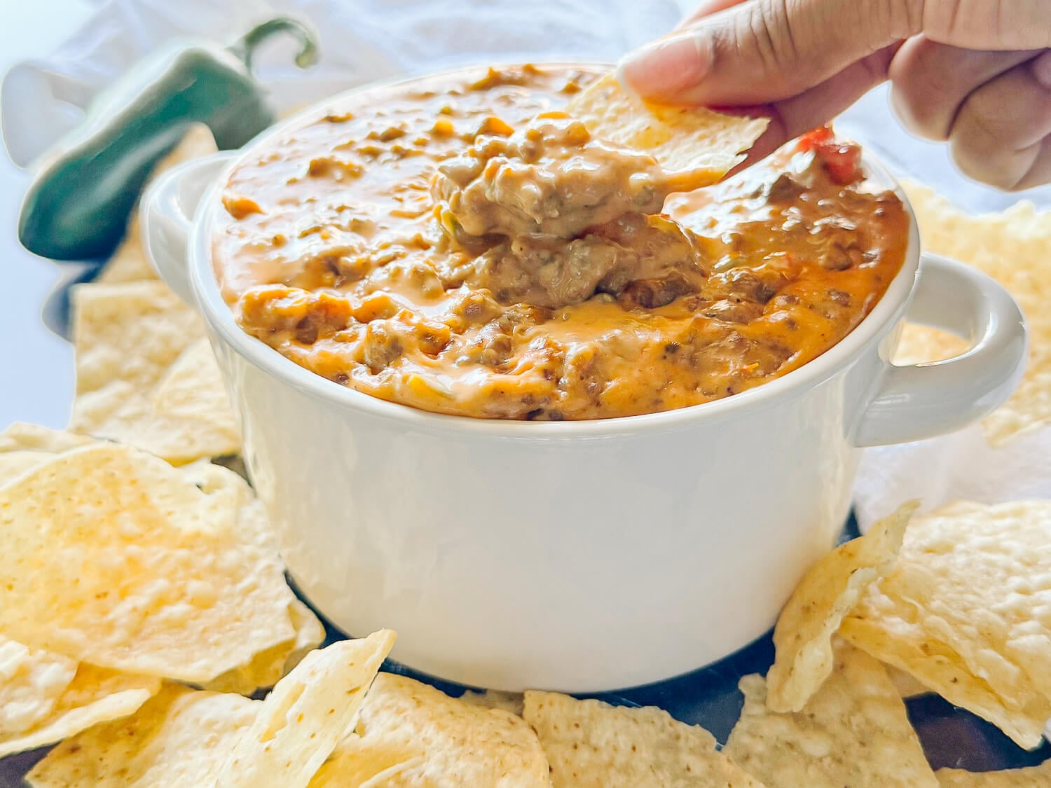 action photo of scooping Sausage Cheese Dip with a tortilla chip in a white bowl