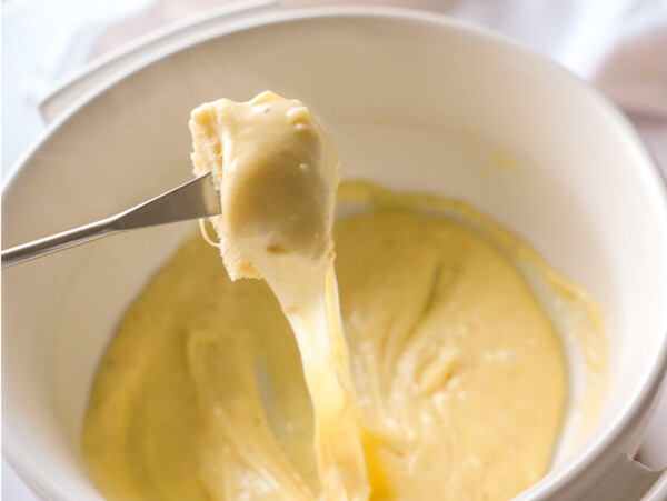 close up photo of Cheese Fondue in a pot and bread on a fondue stick
