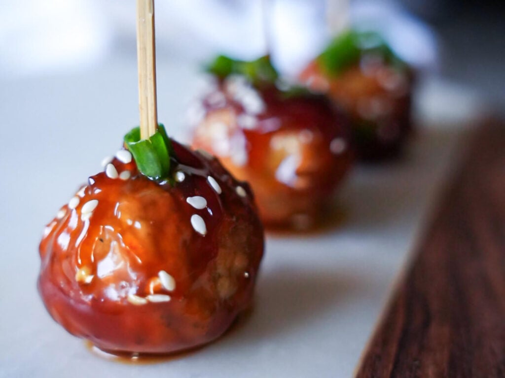 close up photo of a honey garlic meatball on an appetizer tray with a wooden toothpic in the middle