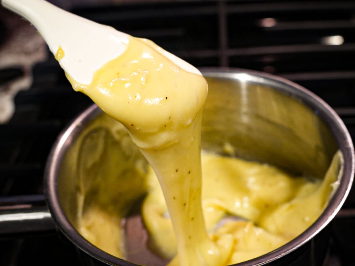 close up photo of melted Cheese Fondue in a sauce pan falling off of a spatula