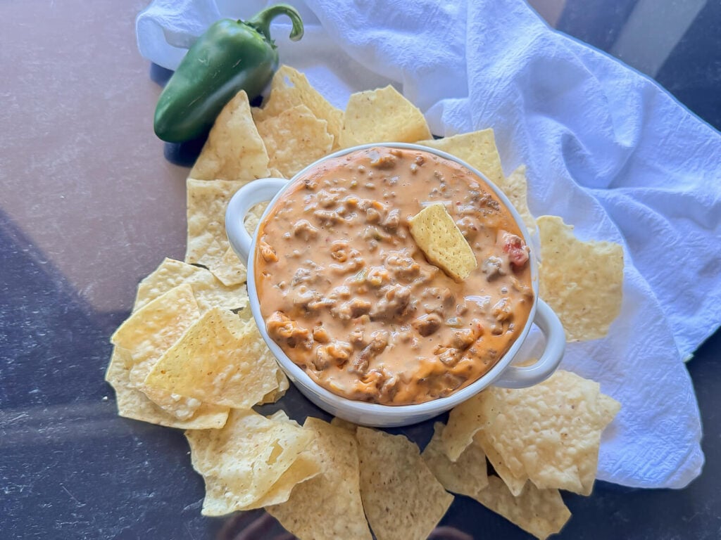overhead photo of Sausage Cheese Dip in a white bowl surrounded by tortilla chips