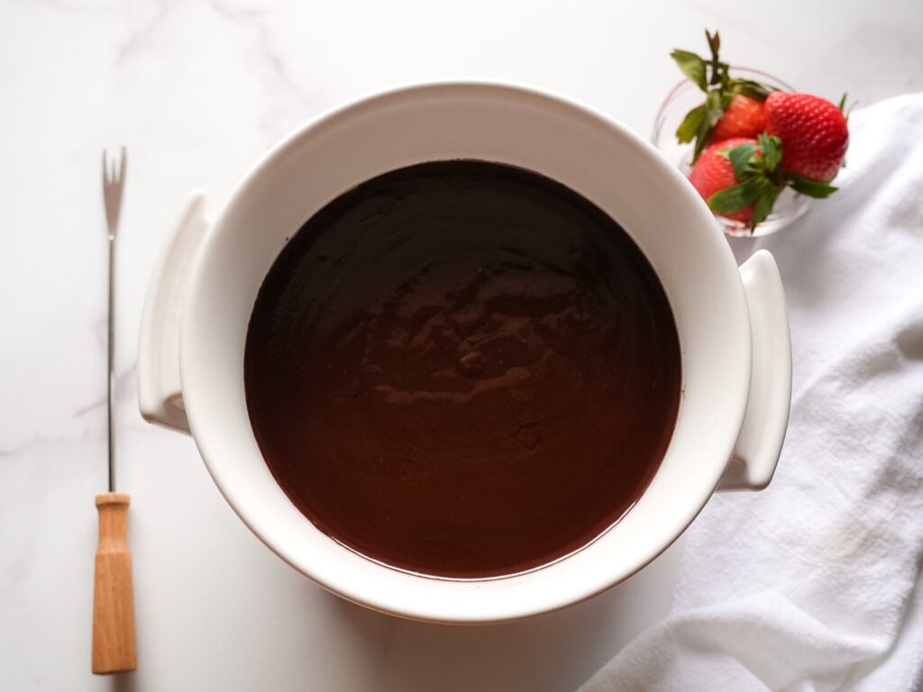 photo of chocolate fondue in a white fondue pot next to a bowl of strawberries