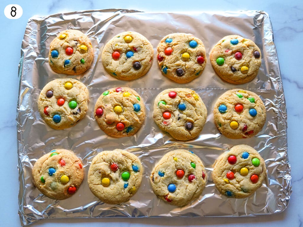 step 8 photo showing M&M cookies resting on a pan with aluminum foil