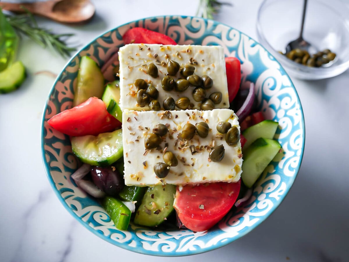 Overhead photo of greek salad with sliced feta and capers on top