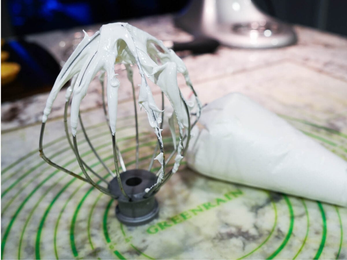 Photo of Swiss Meringue on a whisk next to a bag filled with swiss mergingue