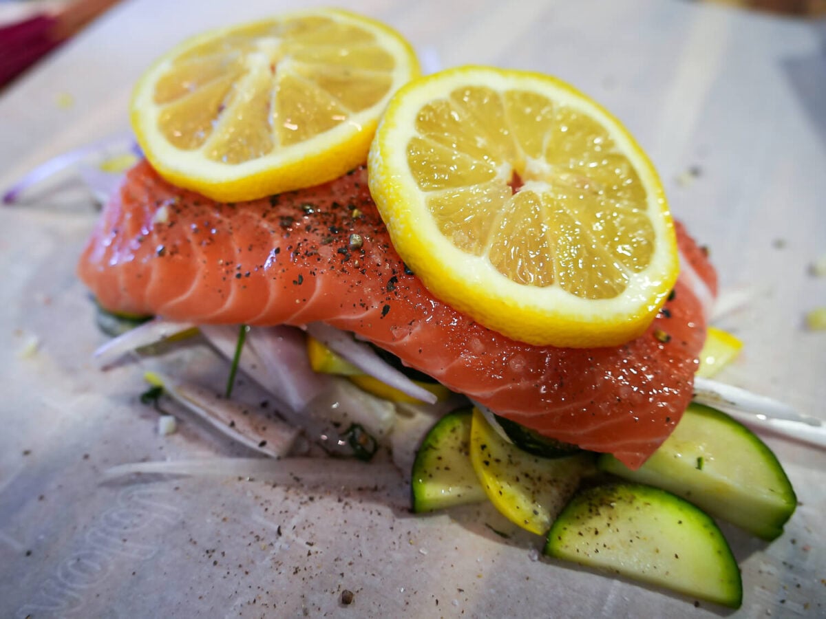 Side photo of salmon with two lemon slices on top of shallots zucchini and squash