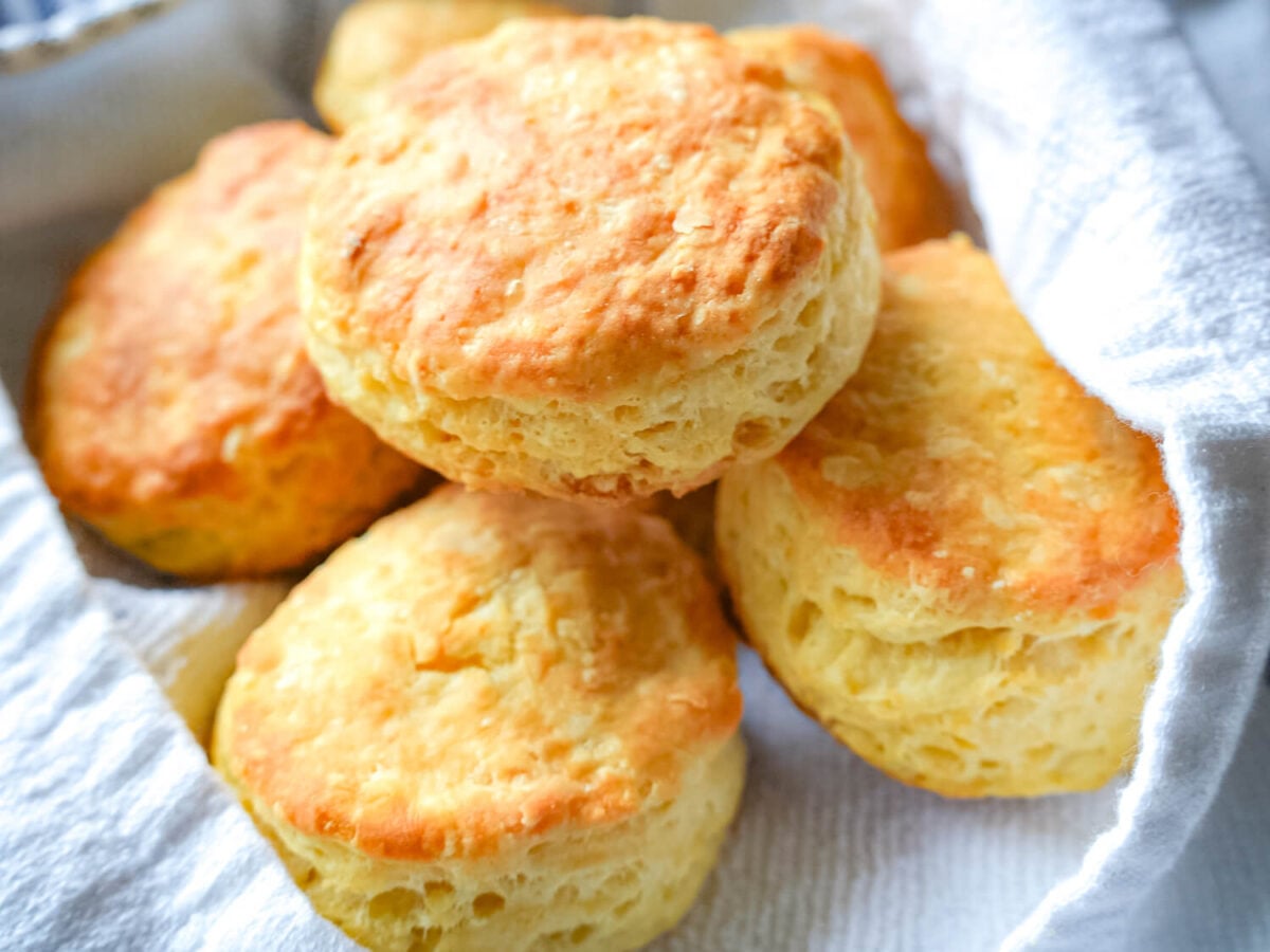 close up photo of a soft buttermilk biscuit sitting on top of other biscuits