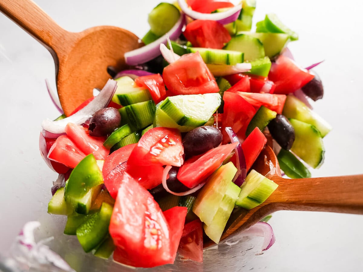 close up photo of tomatoes, red onions, olives, and cucumbers in a glass bowl