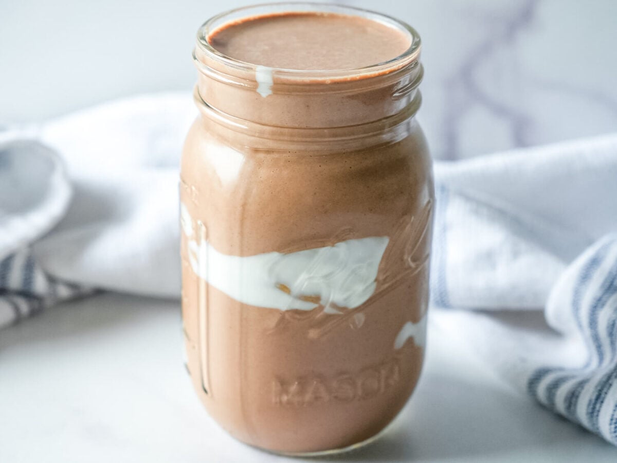 front facing photo of a coffee smoothie in a mason jar with yogurt smeared on the inside for design