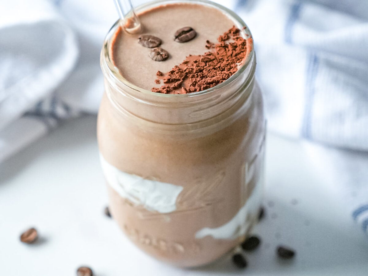 overhead photo of a coffee smoothie with three coffee beans and cocoa on top