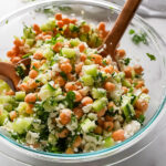 photo of a Chickpea Cucumber Salad in a glass bowl with wooden utensils on a marble surface