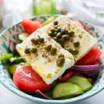 side view of greek salad in a blue and white bowl with a fork