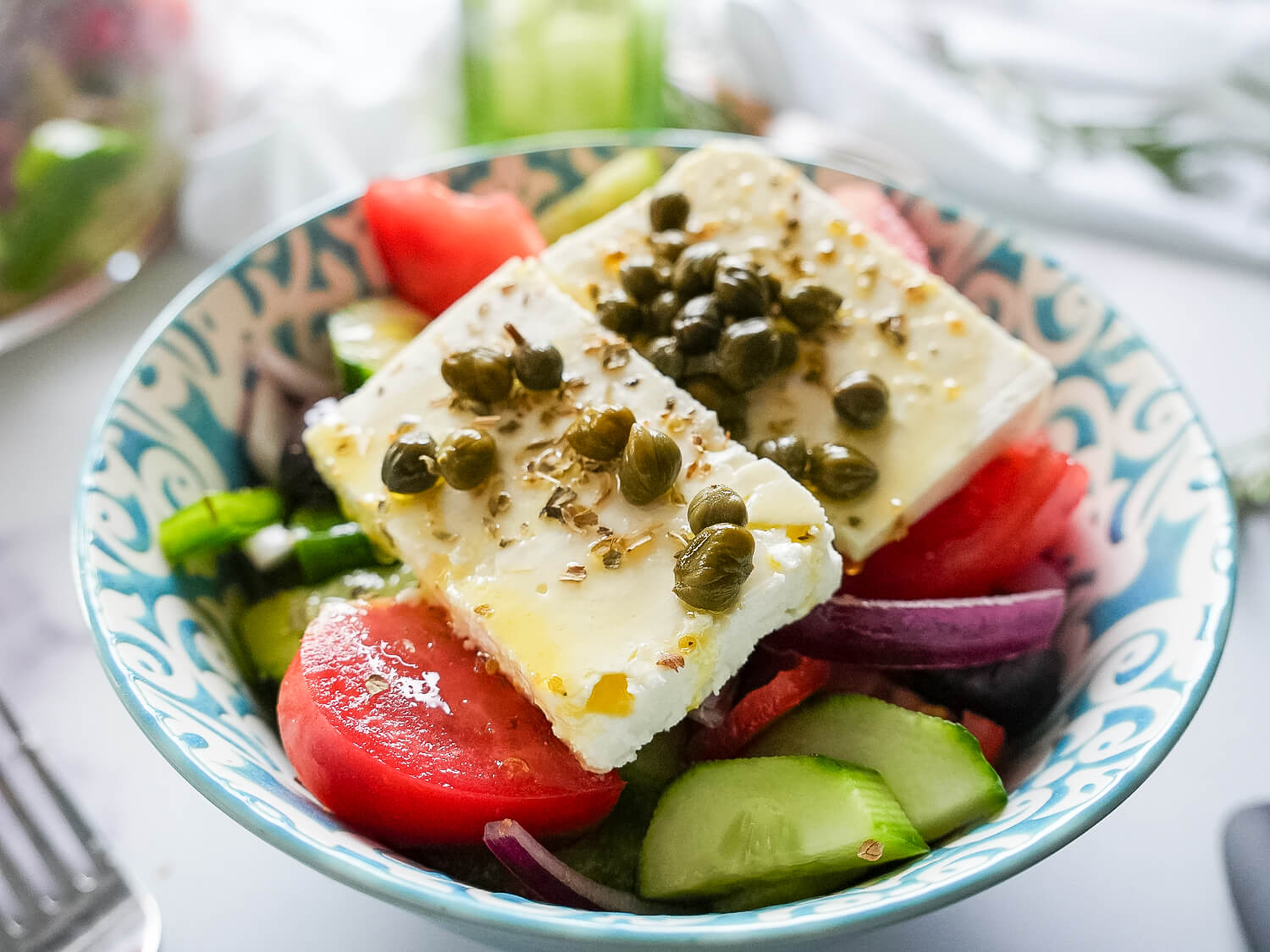 side view of greek salad in a blue and white bowl with a fork